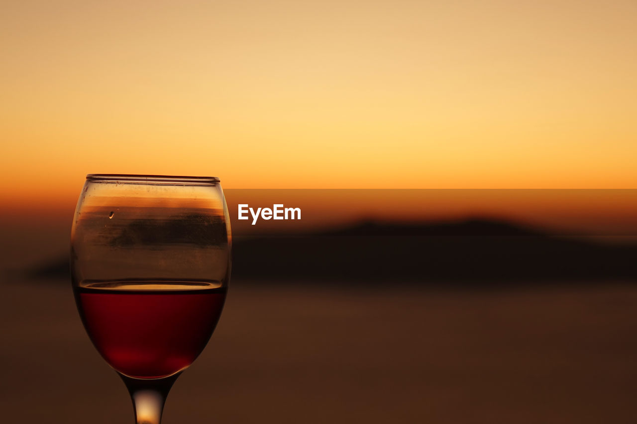 Close-up of wineglass against orange sky during sunset