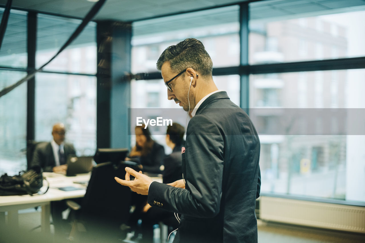 Side view of businessman talking on mobile phone through headphones in office