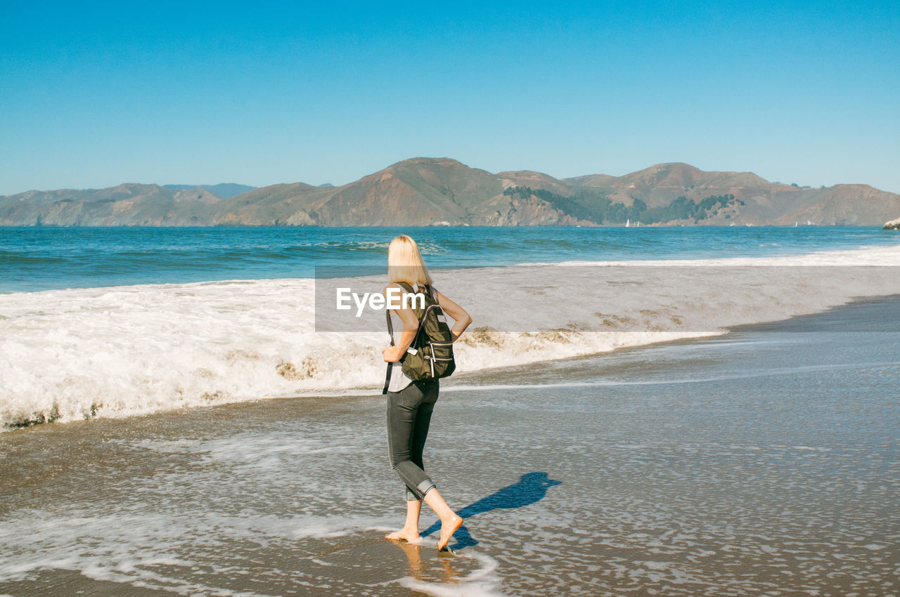 Woman walking at beach against clear sky