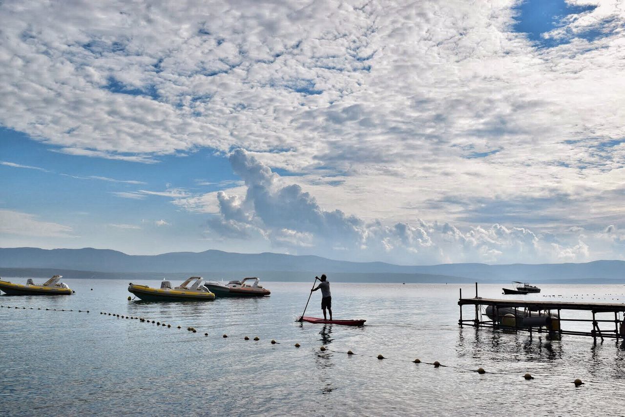 Rear view of person rowing in sea against cloudy sky