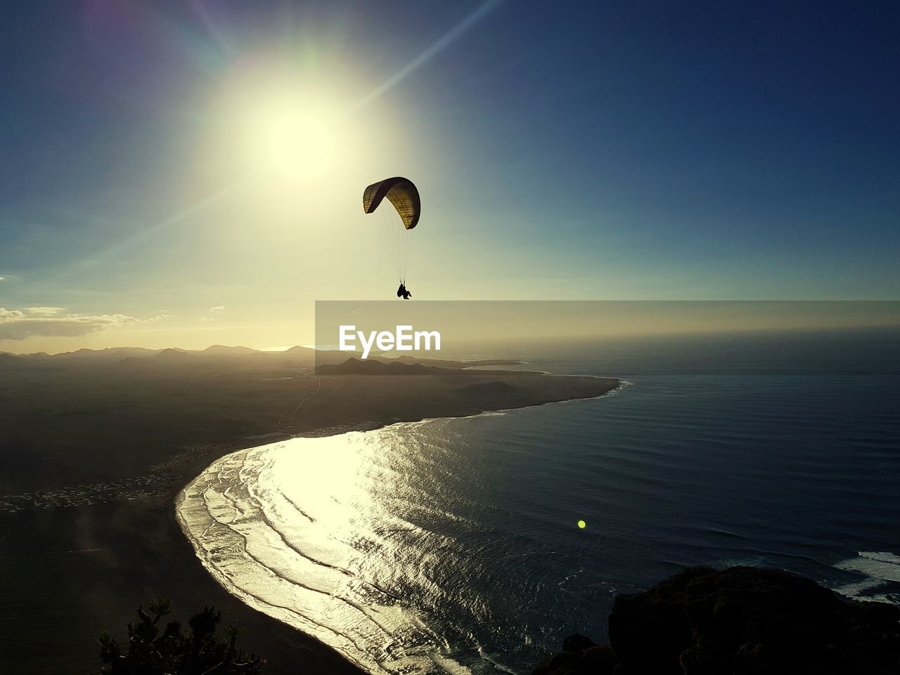 Distant view of person paragliding over seascape against blue sky