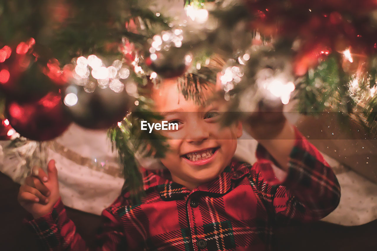 Boy hanging looking at camera under the christmas tree at night time