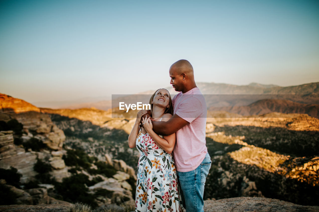 Biracial couple hugging and looking at each other on a mountain top