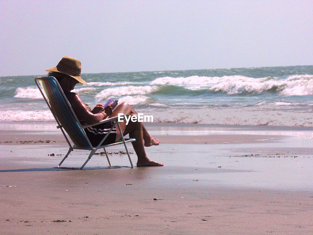 Woman relaxing on chair at beach against clear sky