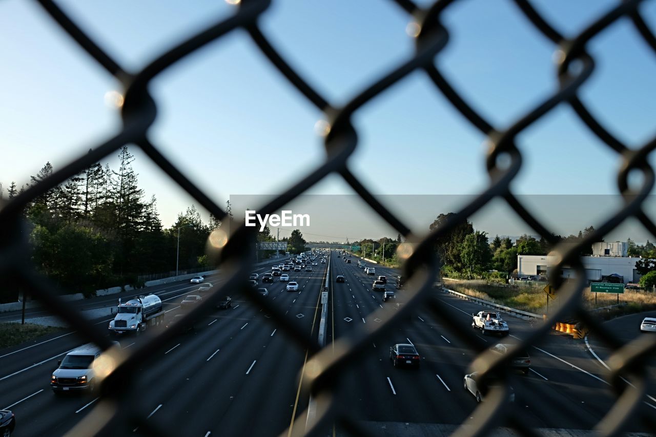 Close-up of cars on road seen through chainlink fence