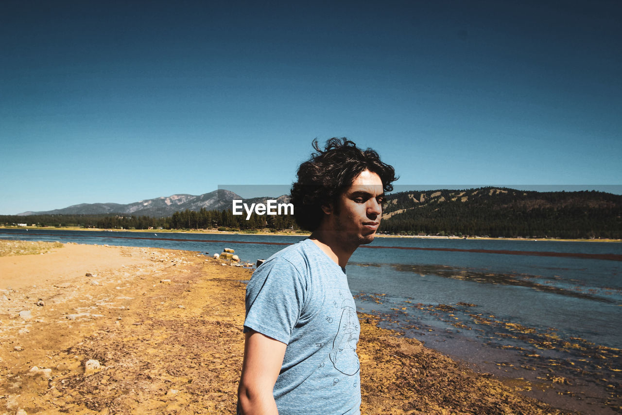 YOUNG MAN LOOKING AWAY AGAINST CLEAR SKY