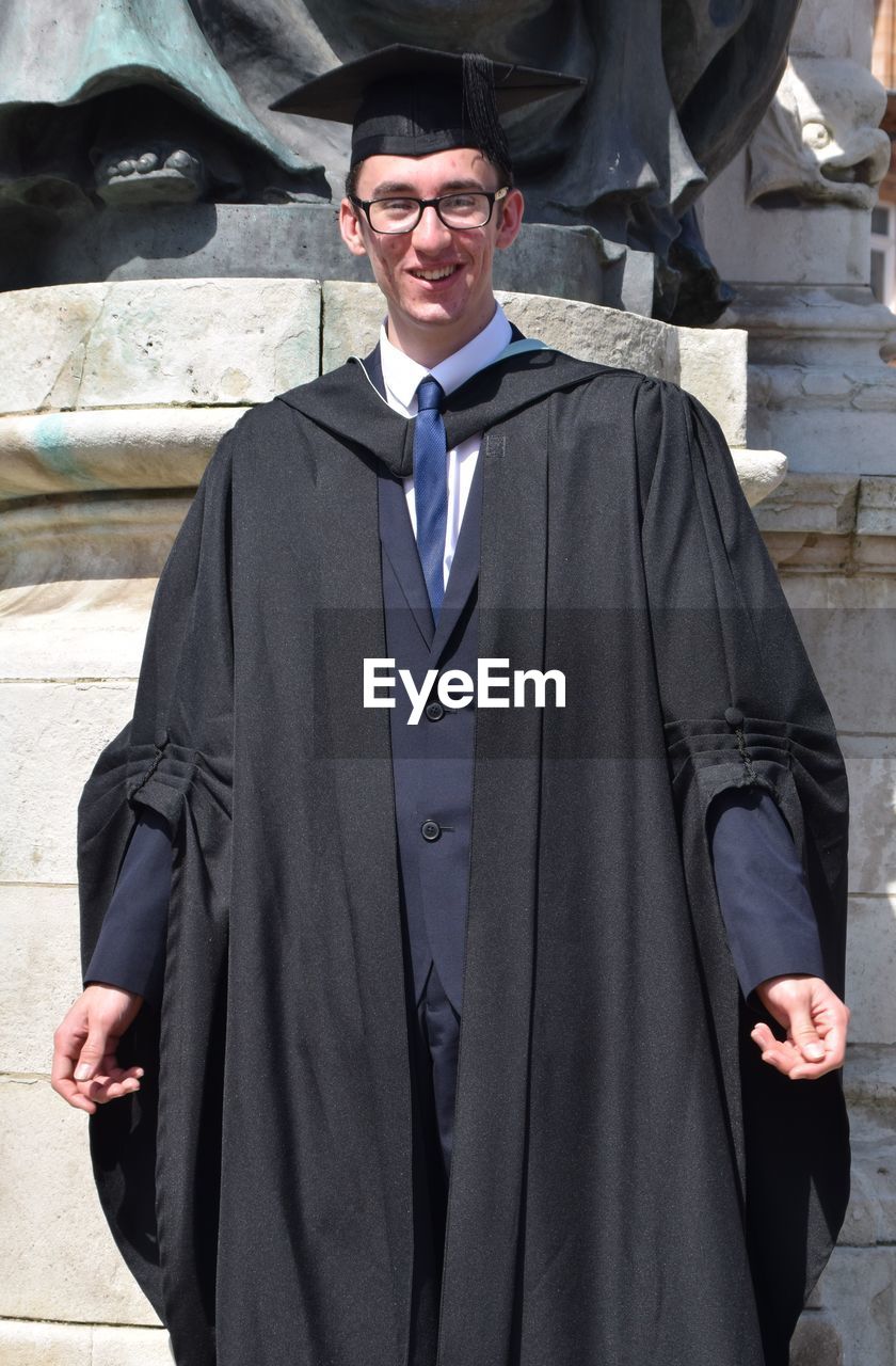 Portrait of smiling man wearing black graduation gown on sunny day