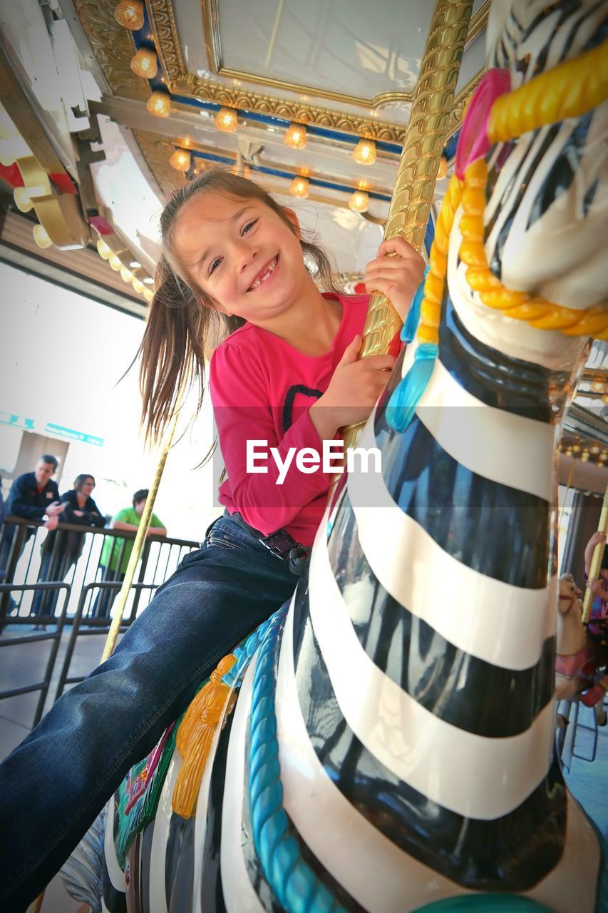 Portrait of happy girl sitting on carousel in amusement park