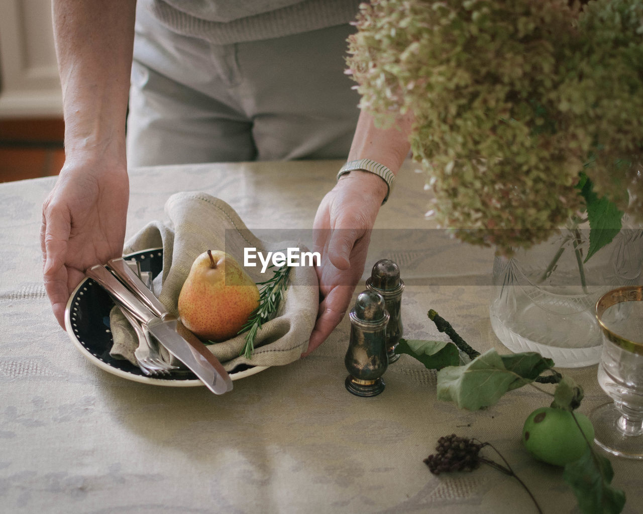 Midsection of man holding pear and rosemary on napkin in plate at table