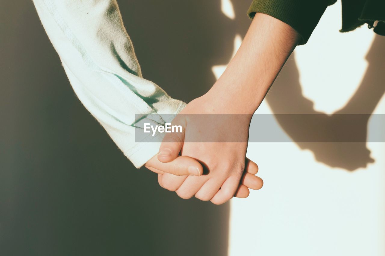 Cropped image of couple holding hands against wall