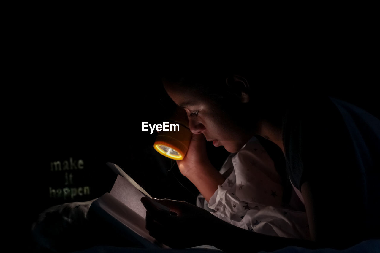 Portrait of girl reading with flashlight 