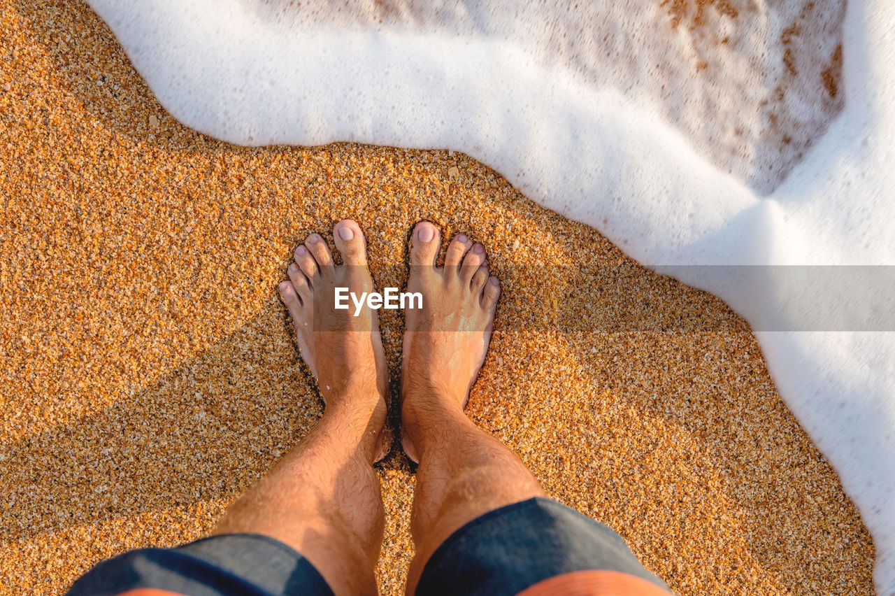 Male feet barefoot on the waves of sea foam on a sandy golden beach on a summer day. top view of