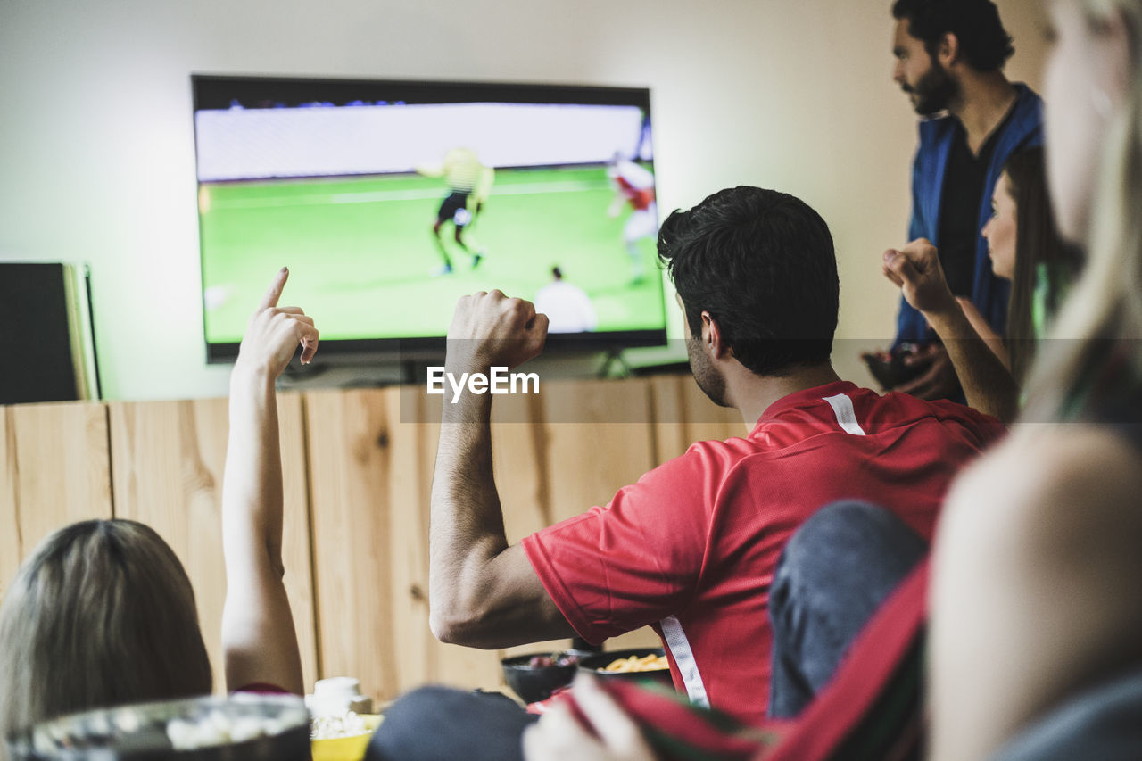 Male and female friends watching soccer match on tv at home