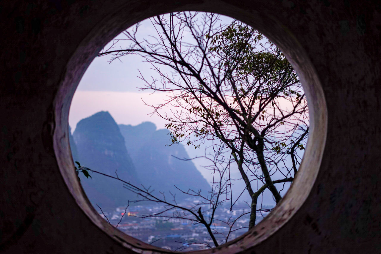 TREES AND MOUNTAINS AGAINST SKY SEEN THROUGH ARCH