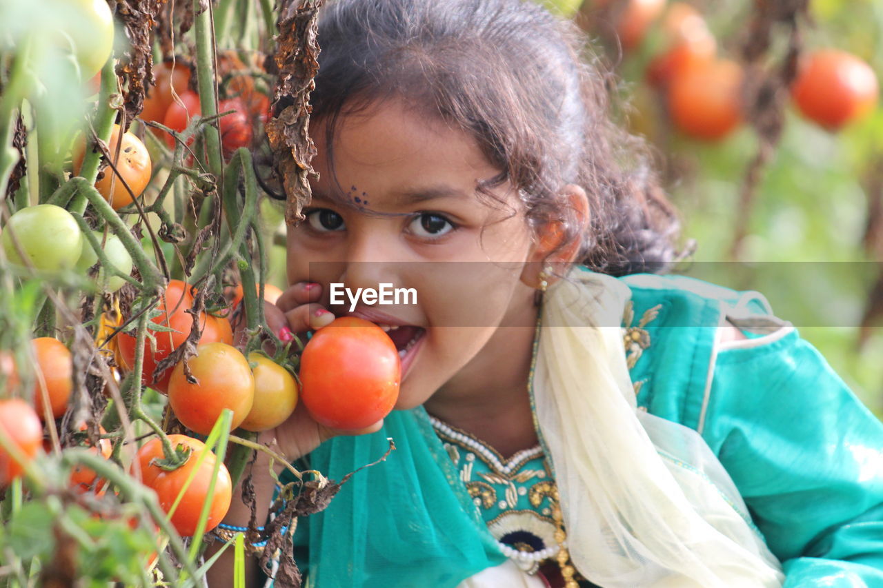 Portrait of girl holding fruits by plant outdoors