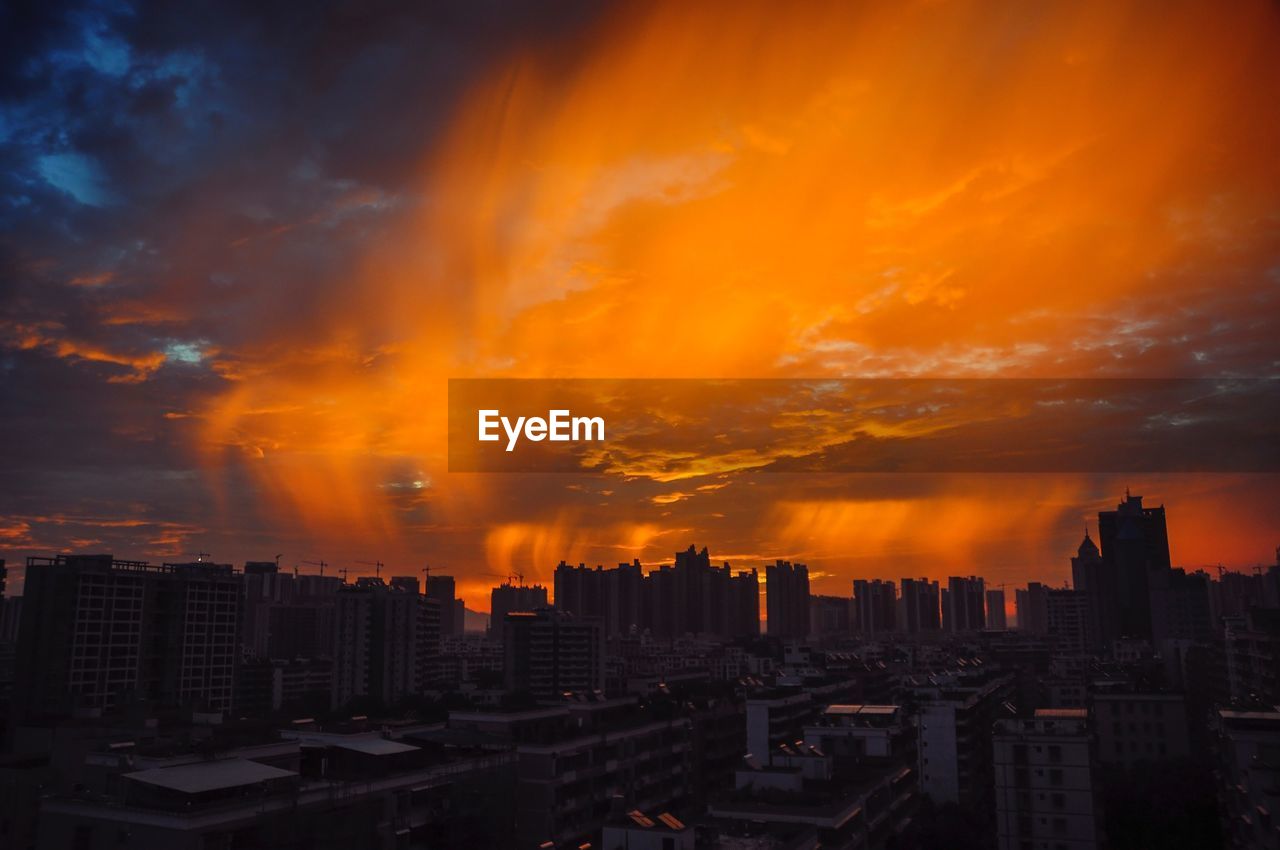 Buildings in city against dramatic sky during sunset