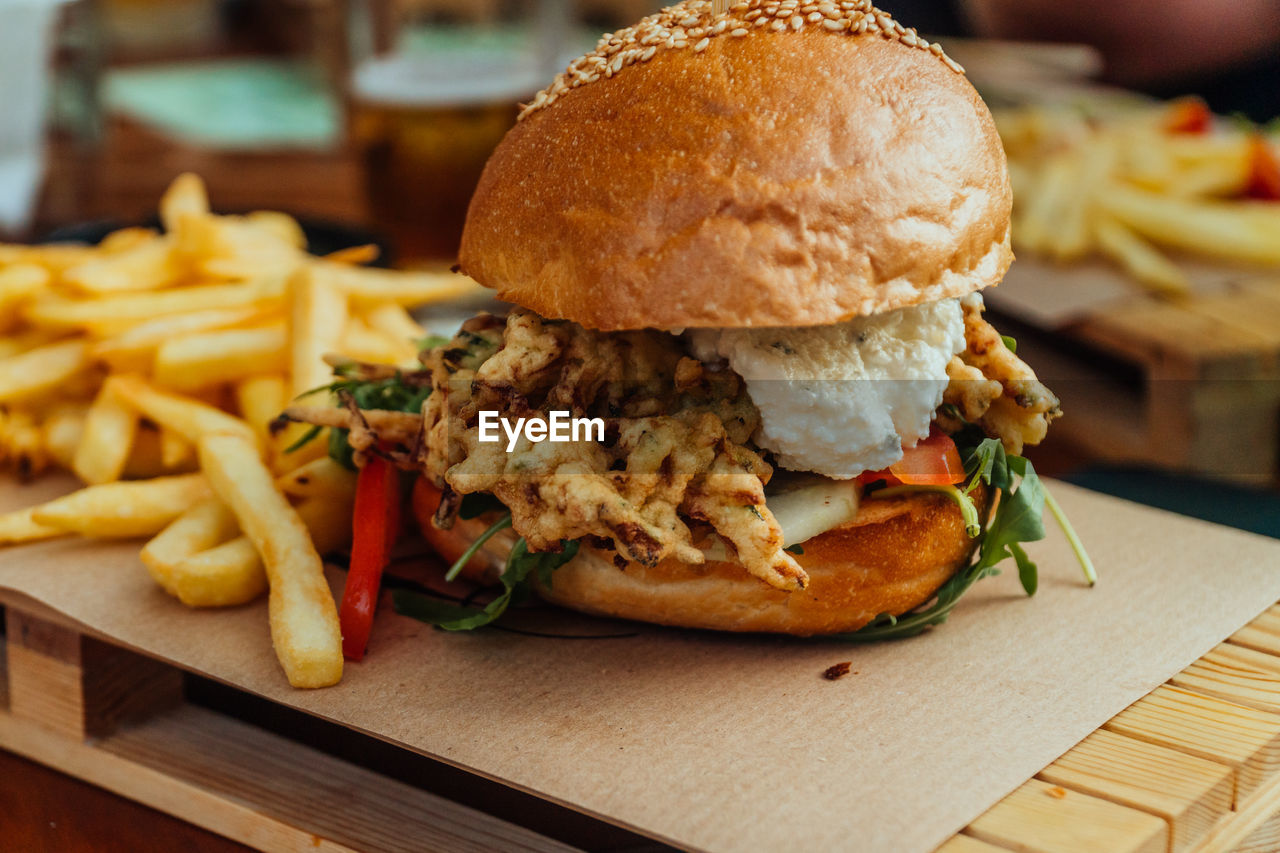 Close-up of veggie burger made of zucchini with golden bun and french fries on a wooden platter.