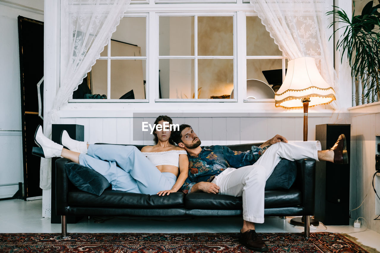 Young stylish couple sitting on sofa indoors