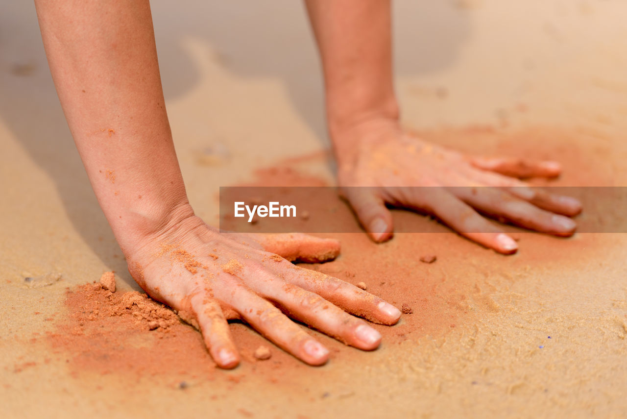 Cropped image of hands playing with sand at beach