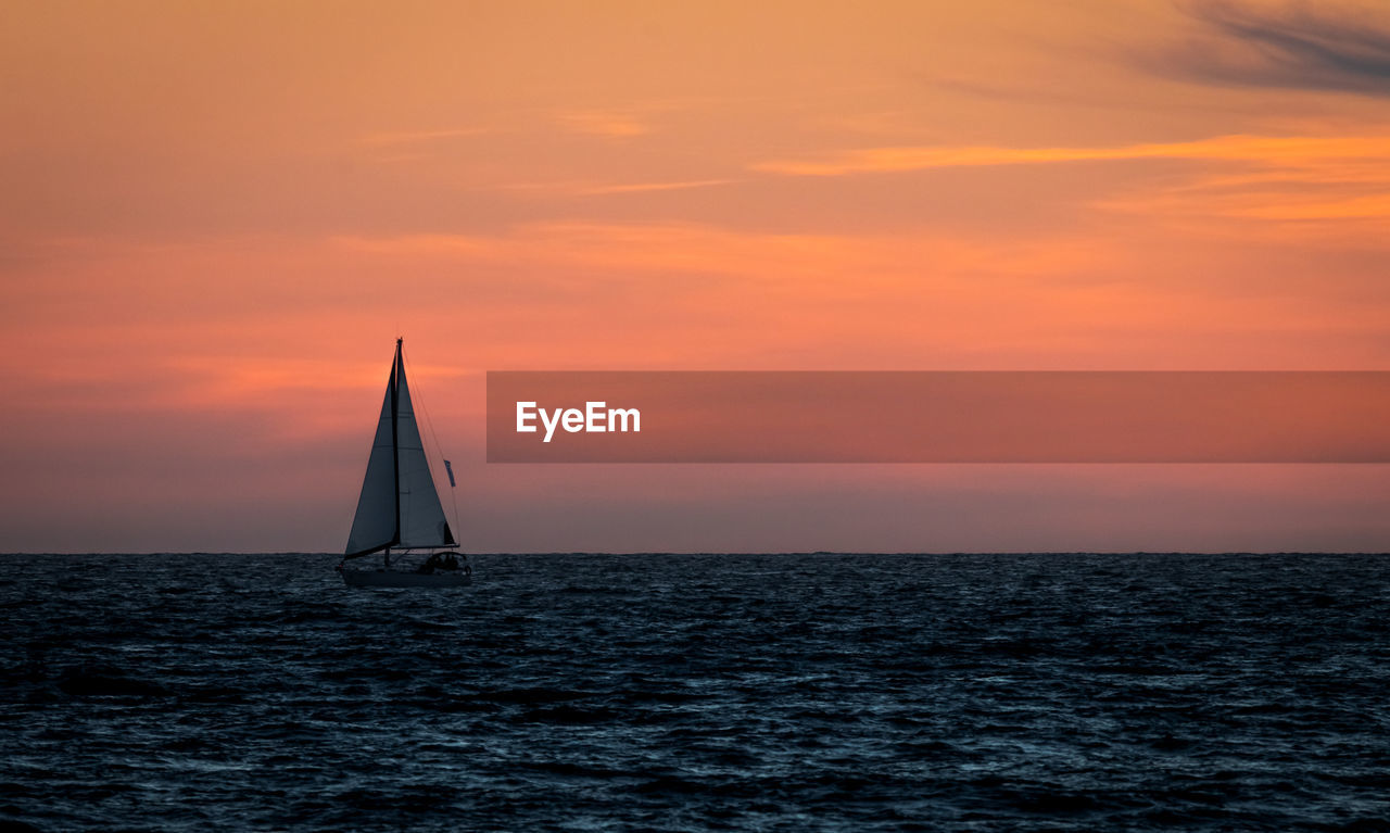 Sailboat sailing on sea against orange sky