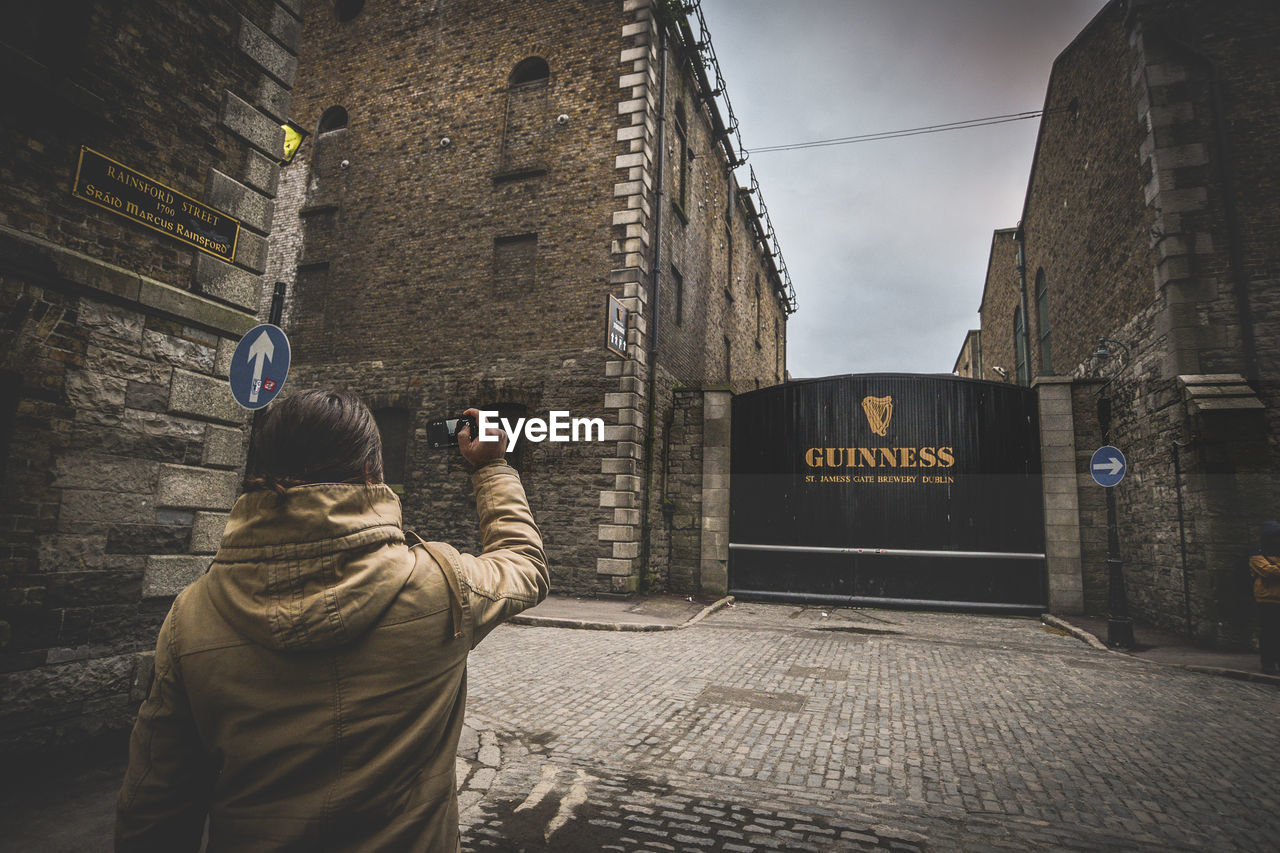 REAR VIEW OF MAN PHOTOGRAPHING AT STREET