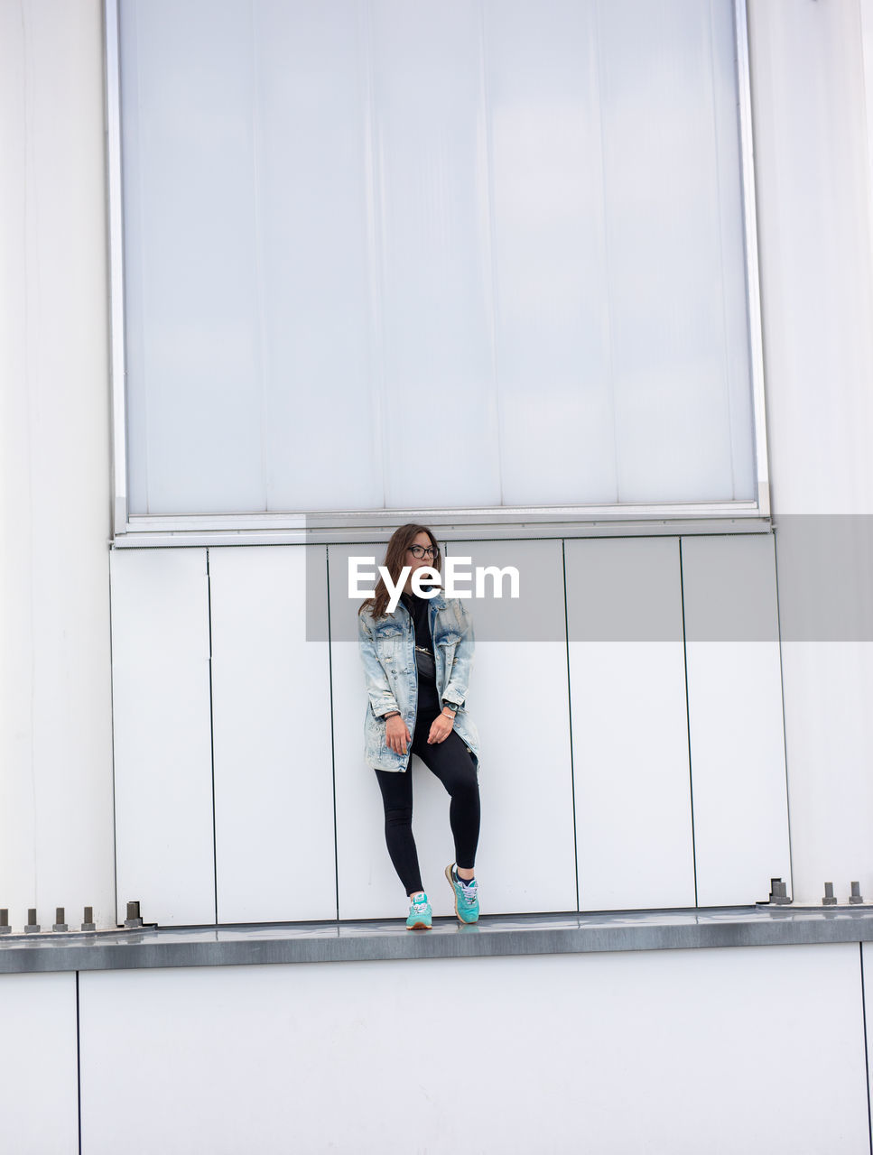 YOUNG WOMAN STANDING AGAINST WALL