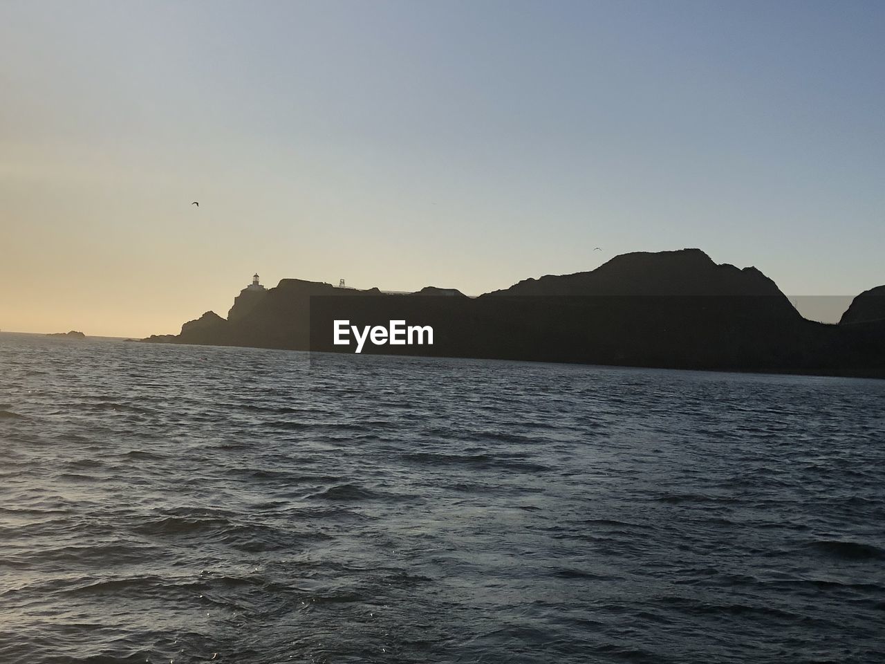 SCENIC VIEW OF SEA BY SILHOUETTE MOUNTAIN AGAINST CLEAR SKY