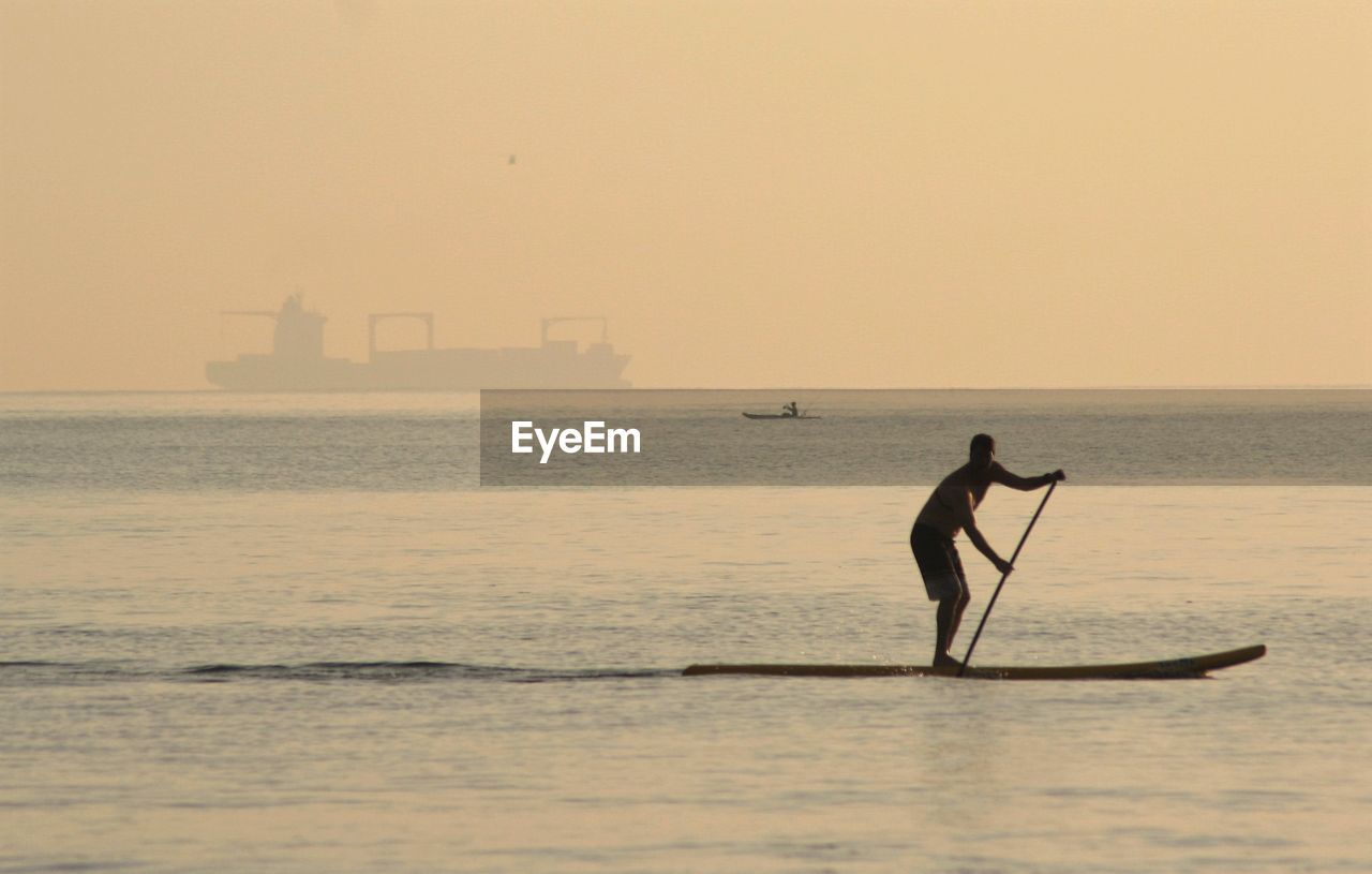 Man paddleboarding in sea against sky