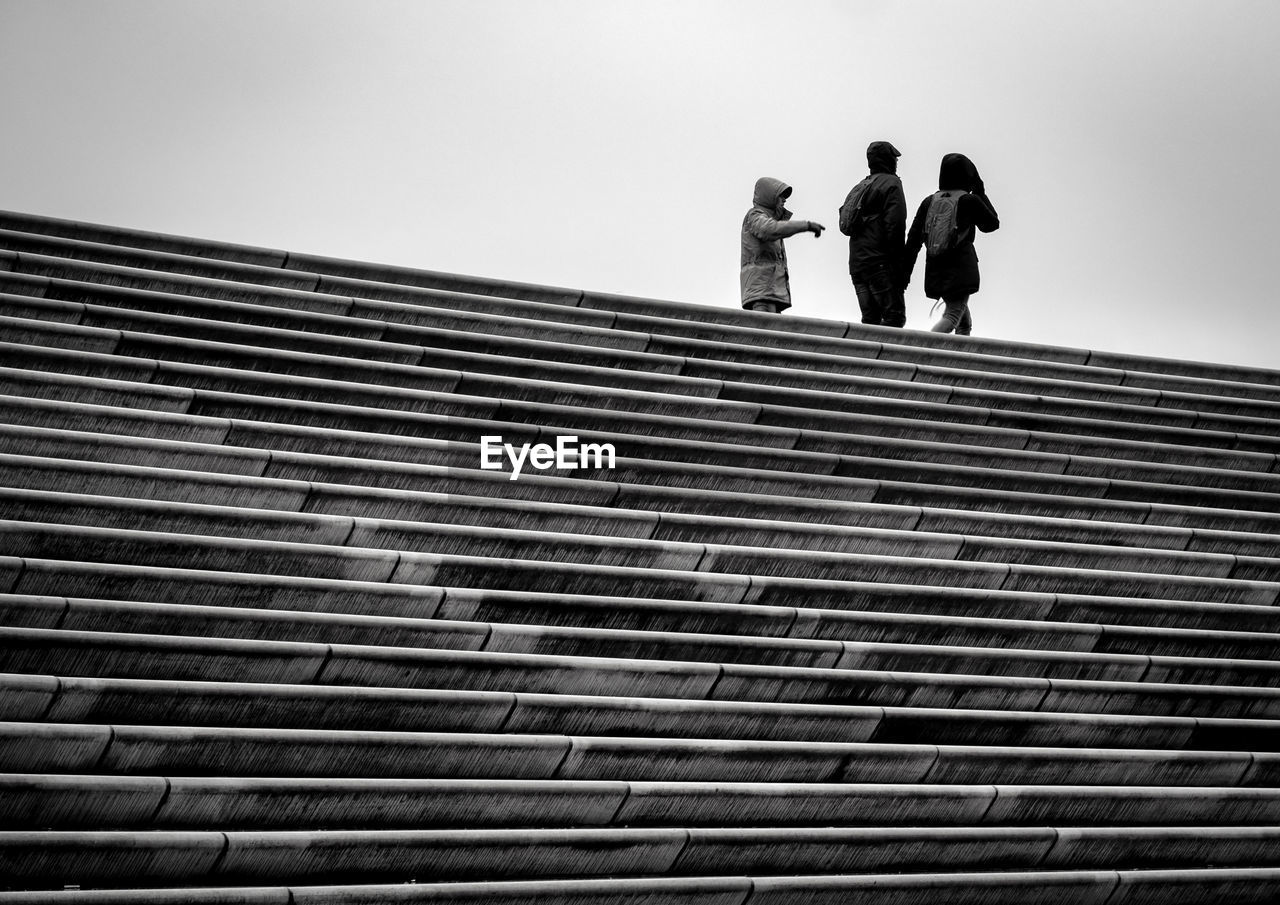 LOW ANGLE VIEW OF MEN ON ROOF AGAINST SKY