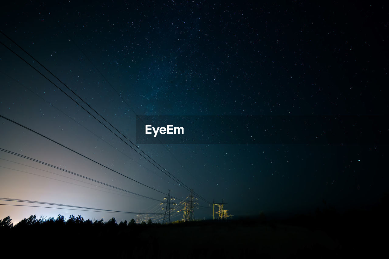 Silhouette electricity pylons against sky at night