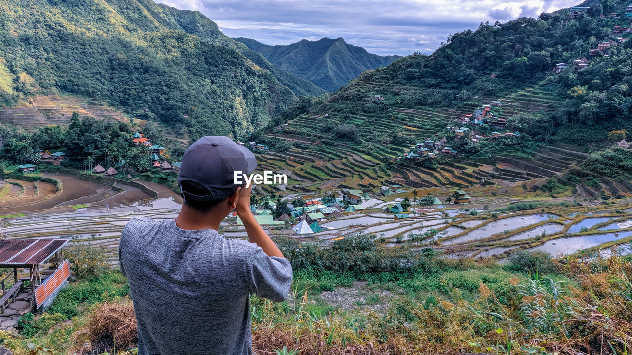 Rear view of man taking a photo of mountains