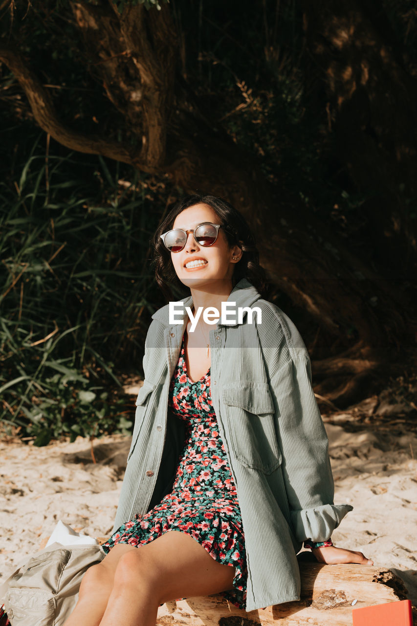 portrait of young woman wearing sunglasses while sitting on field