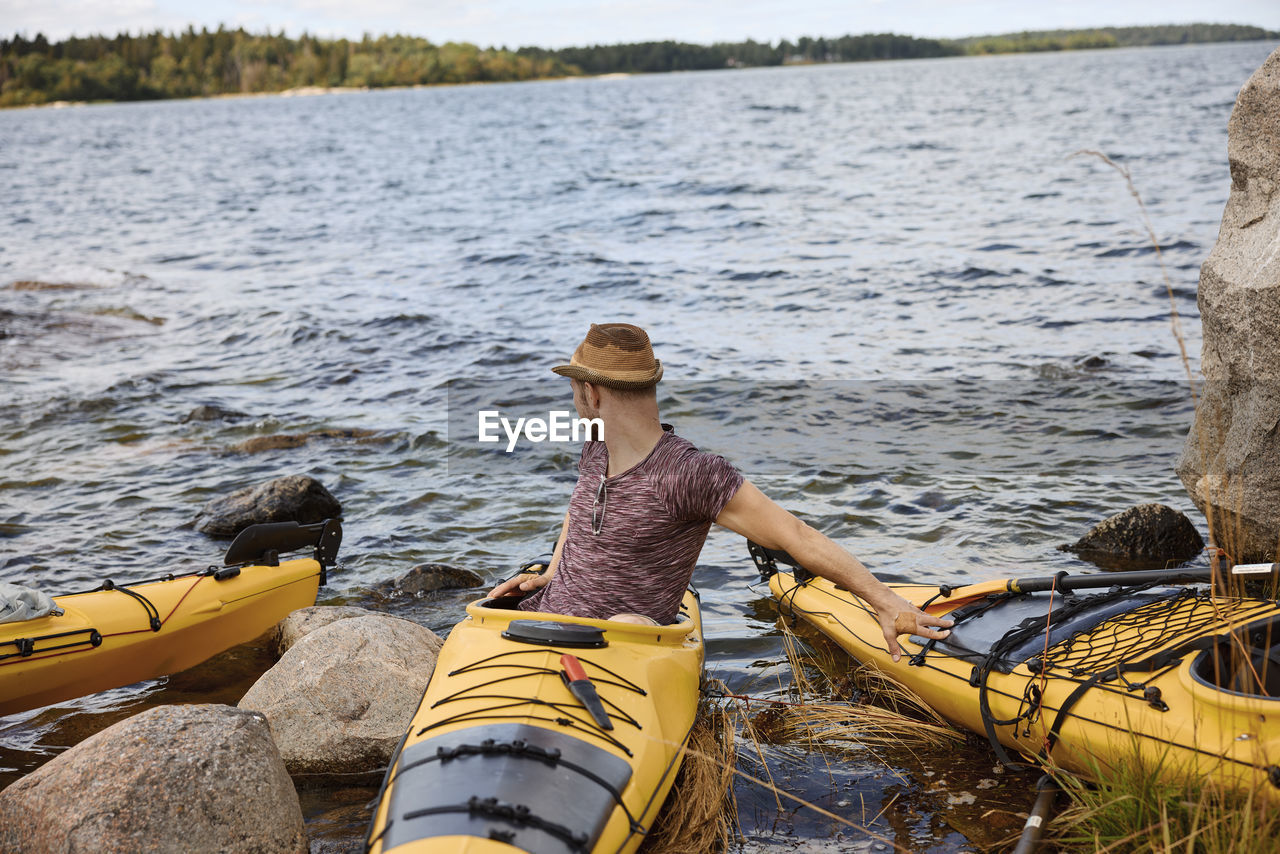 Man sitting on kayak on coast and looking away
