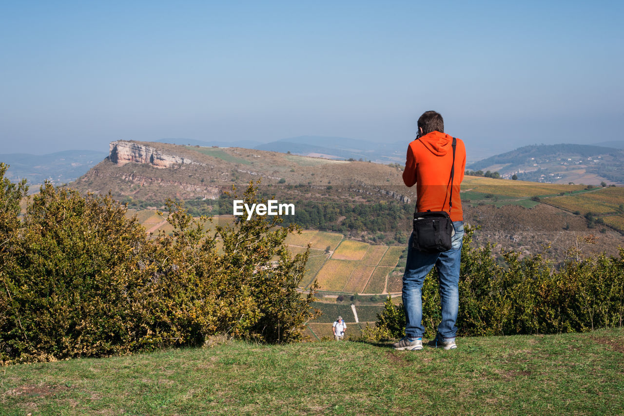Rear view of young man standing on mountain against clear sky