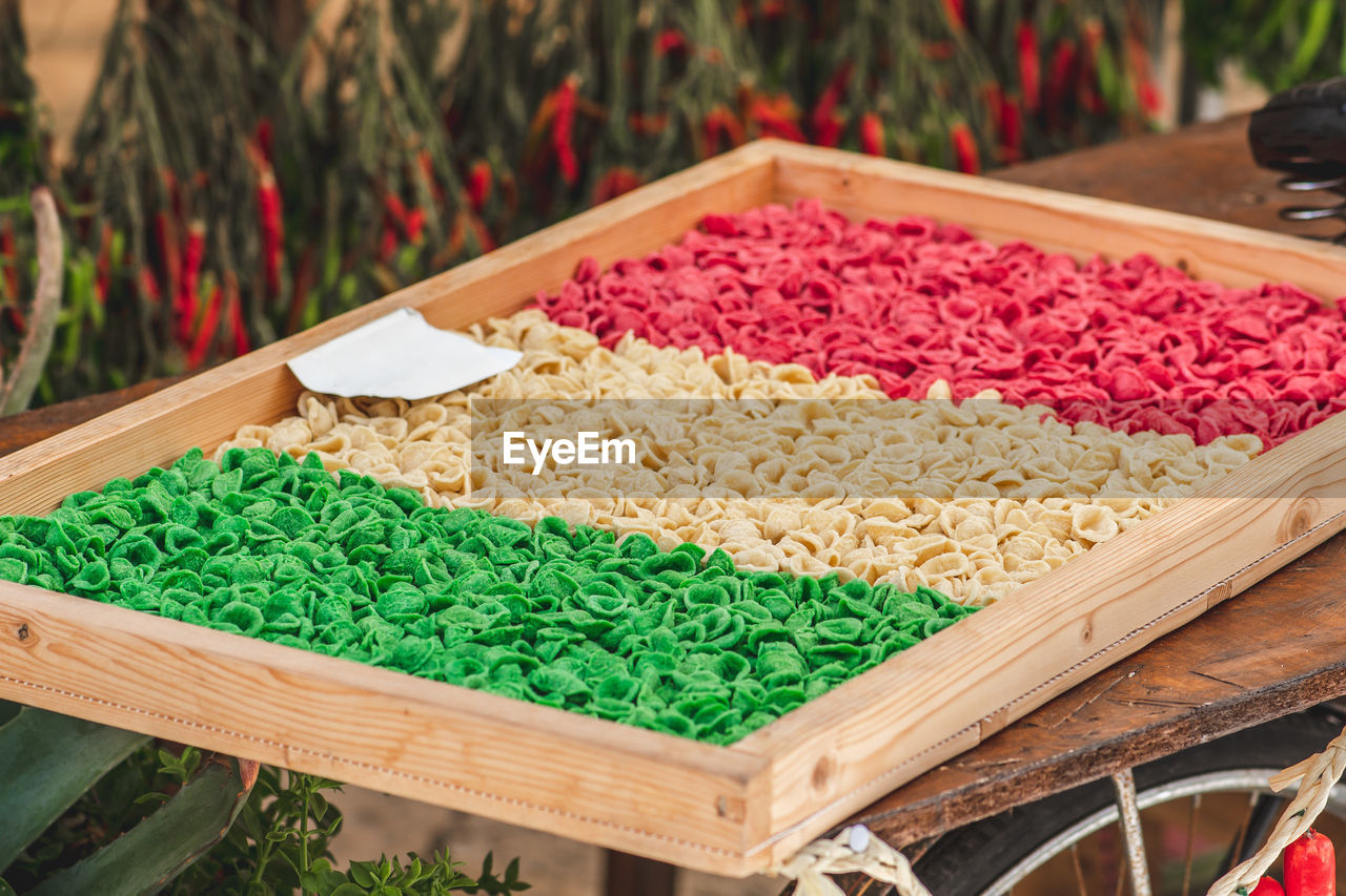 Fresh green, white and red orecchiette or orecchietta pasta drying under the sun on a wooden board