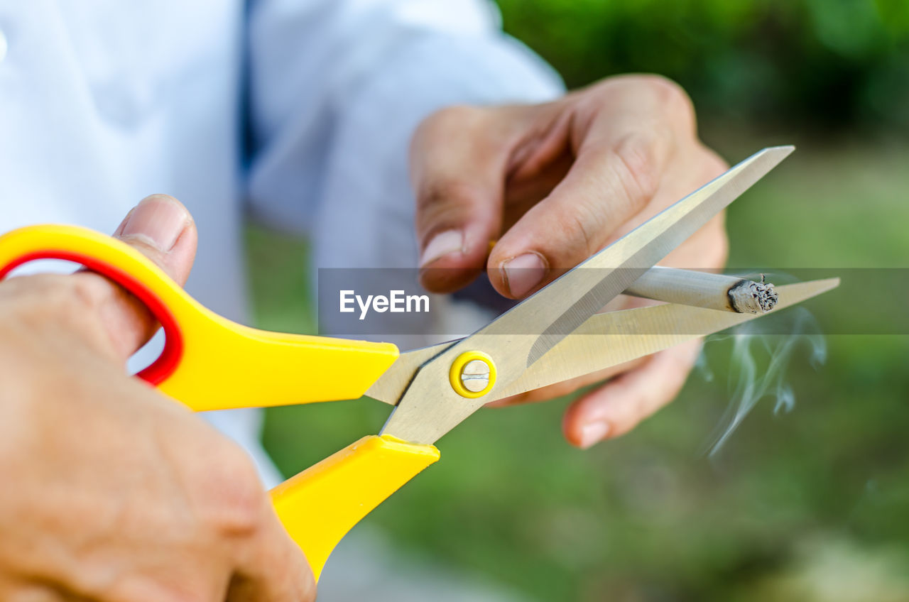 Midsection of man cutting cigarette with scissors