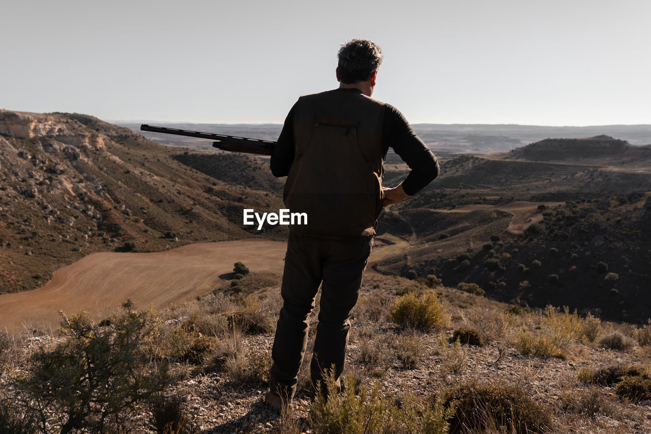 rear view of man standing on mountain against clear sky