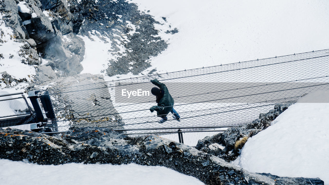 High angle view of man crossing footbridge over snow covered landscape