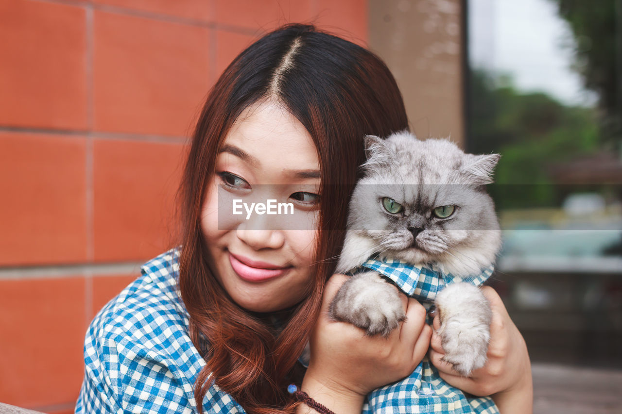 Close-up of thoughtful young woman holding cat against brick wall
