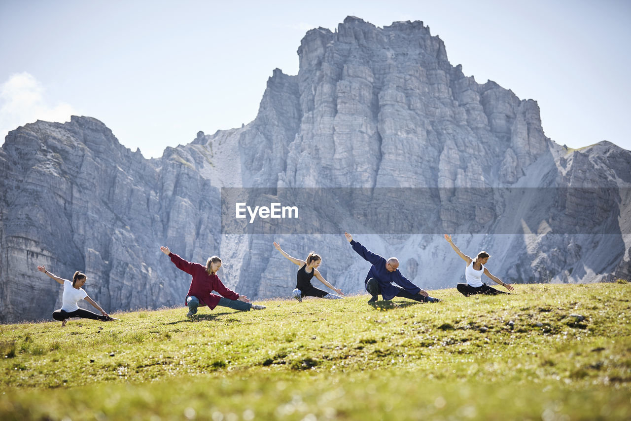 Active man and women practicing stretching exercise against mountain