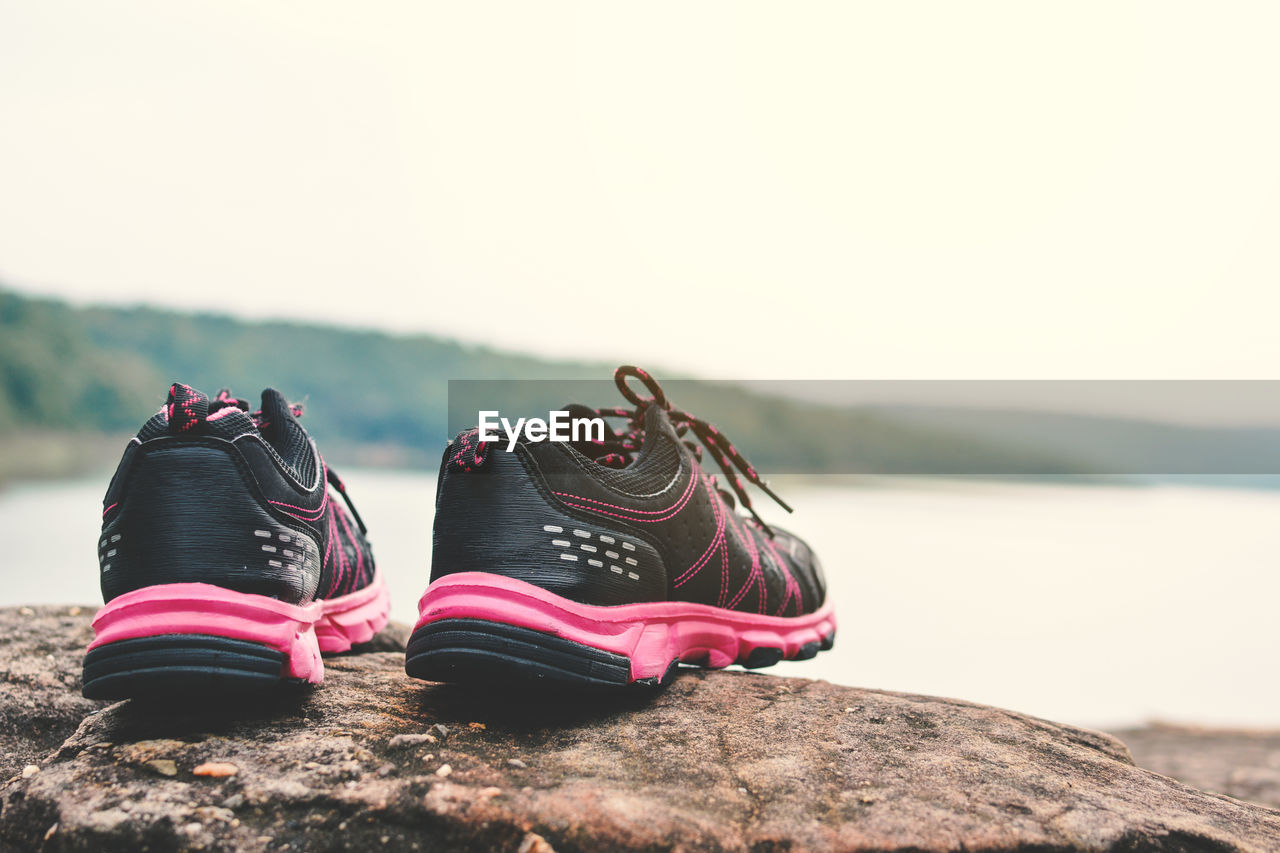 Black shoes on rock by lake against sky