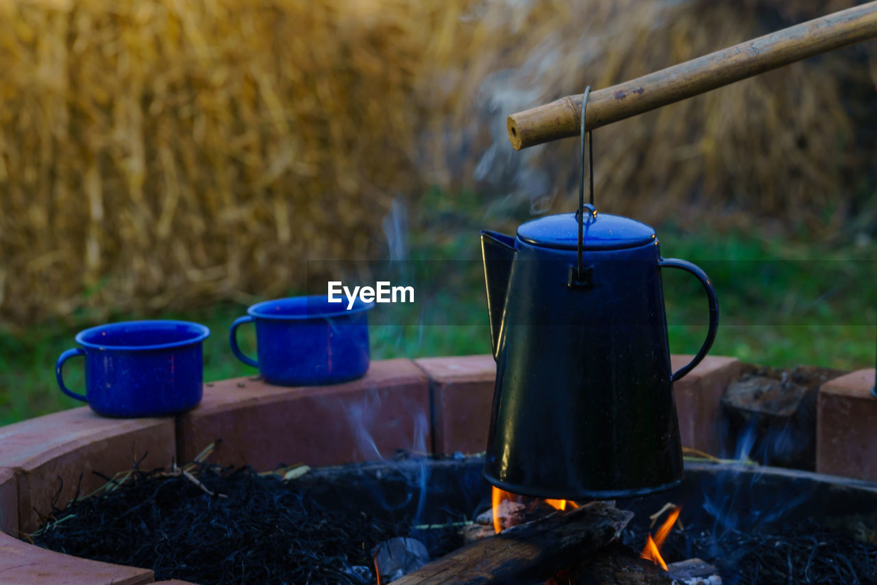 heat, burning, fire, nature, kitchen utensil, food and drink, household equipment, flame, camping, kettle, food, no people, wood, plant, blue, day, cooking pan, grass, container, outdoors, focus on foreground, teapot, camping stove, metal, tea, appliance, iron, drink, backyard, hot drink