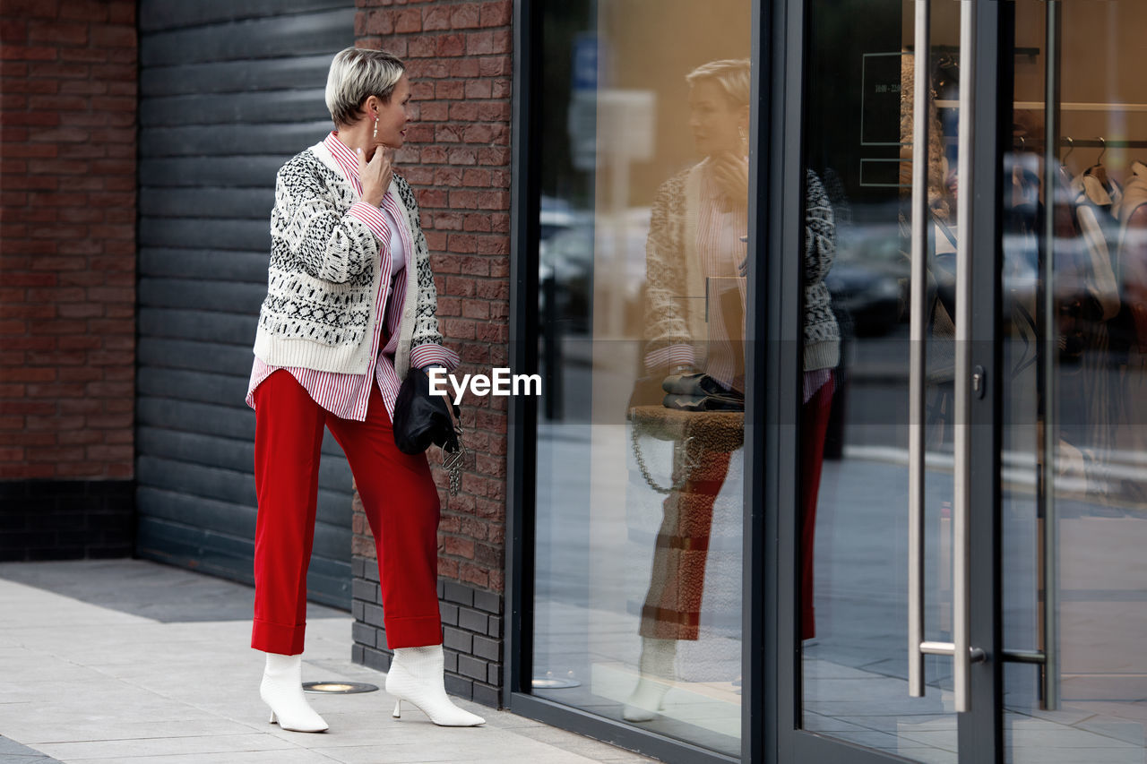 Fashionably dressed woman shopping, looking at reflection in mirror of shop window outside