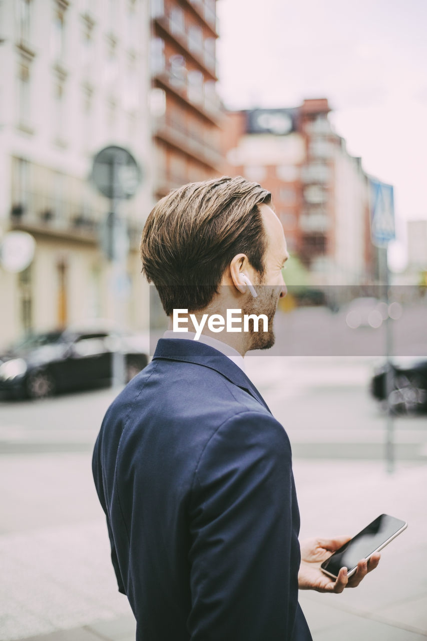 Side view of businessman talking through headphones in city