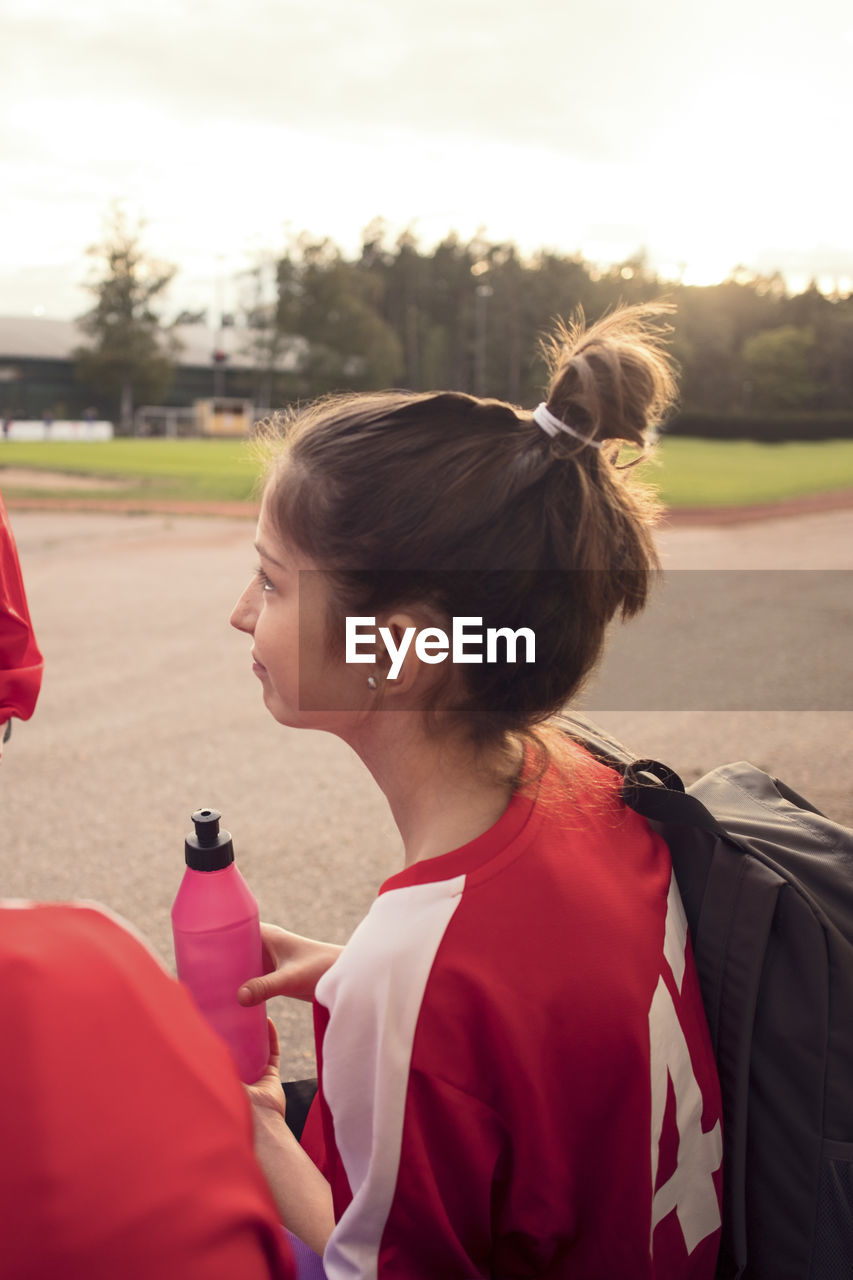 Side view of girl sitting by friends against soccer field