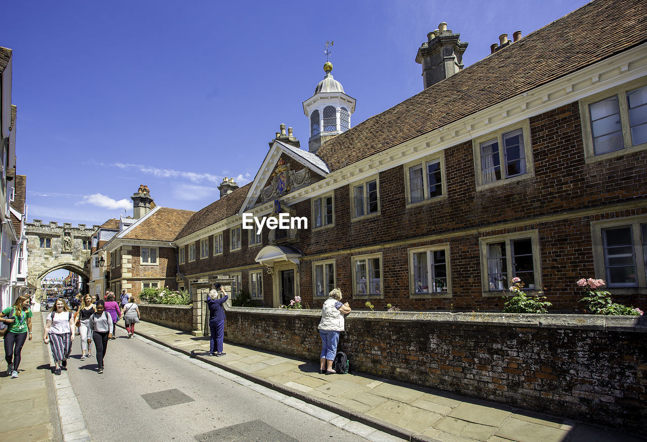 PEOPLE WALKING BY BUILDINGS IN CITY AGAINST SKY