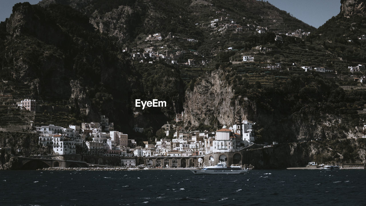 Trees and buildings by sea against mountain