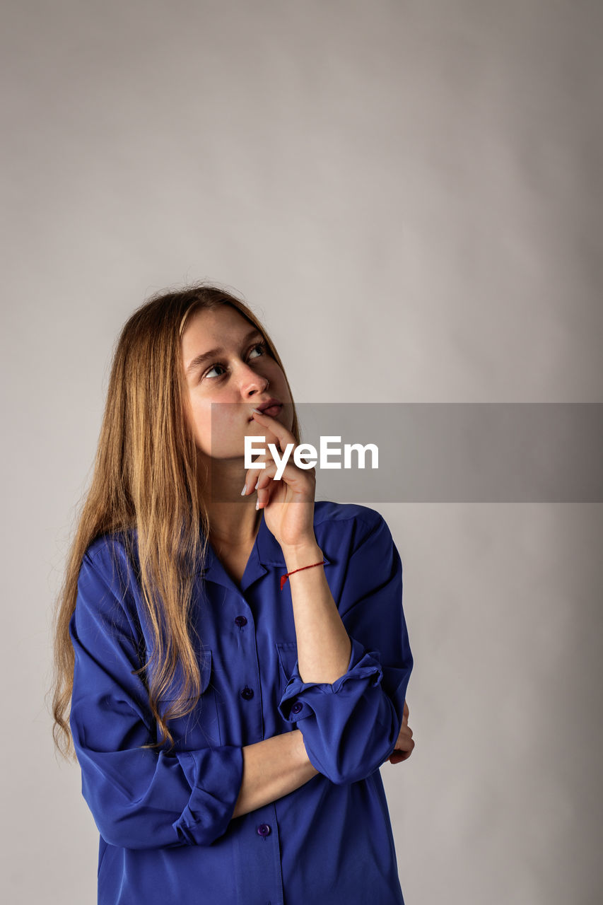 PORTRAIT OF BEAUTIFUL YOUNG WOMAN AGAINST BLUE BACKGROUND