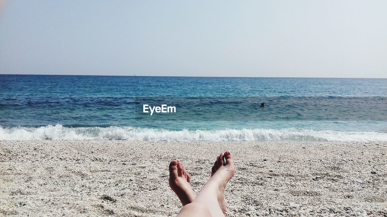 Low section of woman at beach against clear sky