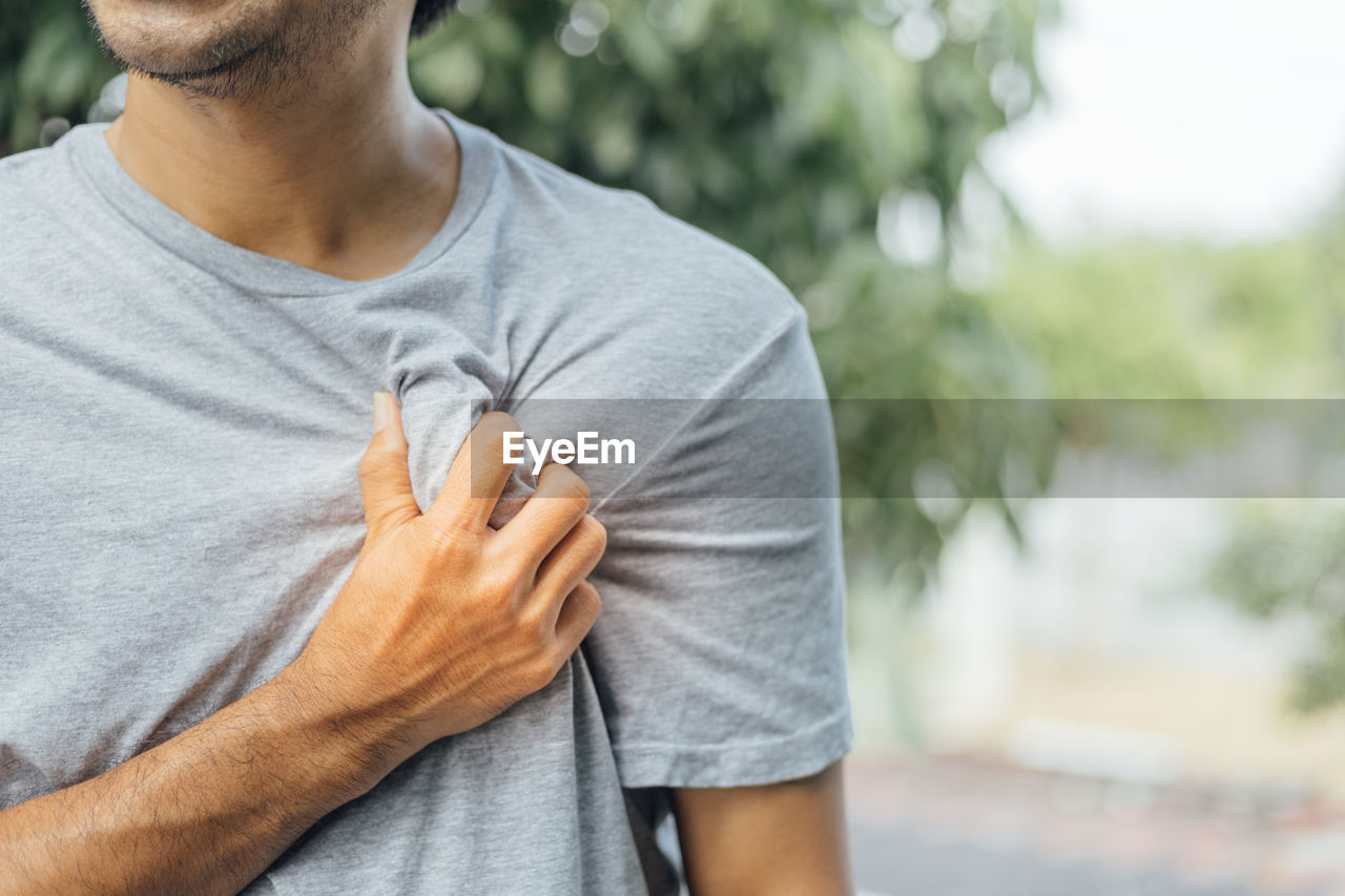 Midsection of man touching chest in pain while standing against trees